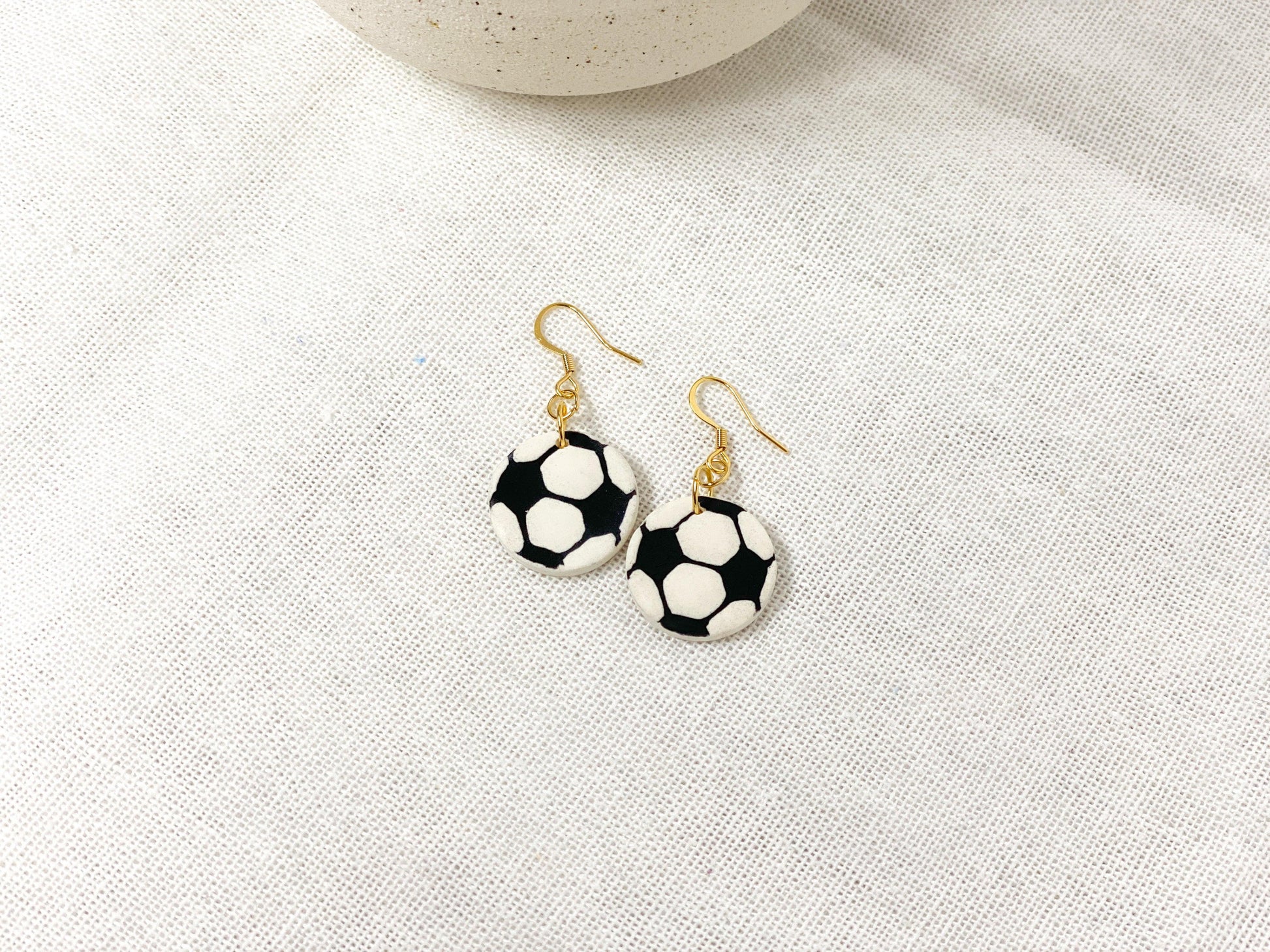 Handmade Soccer Earrings with Gold Surgical Steel Ear Wires laying flat on White Linen Cloth