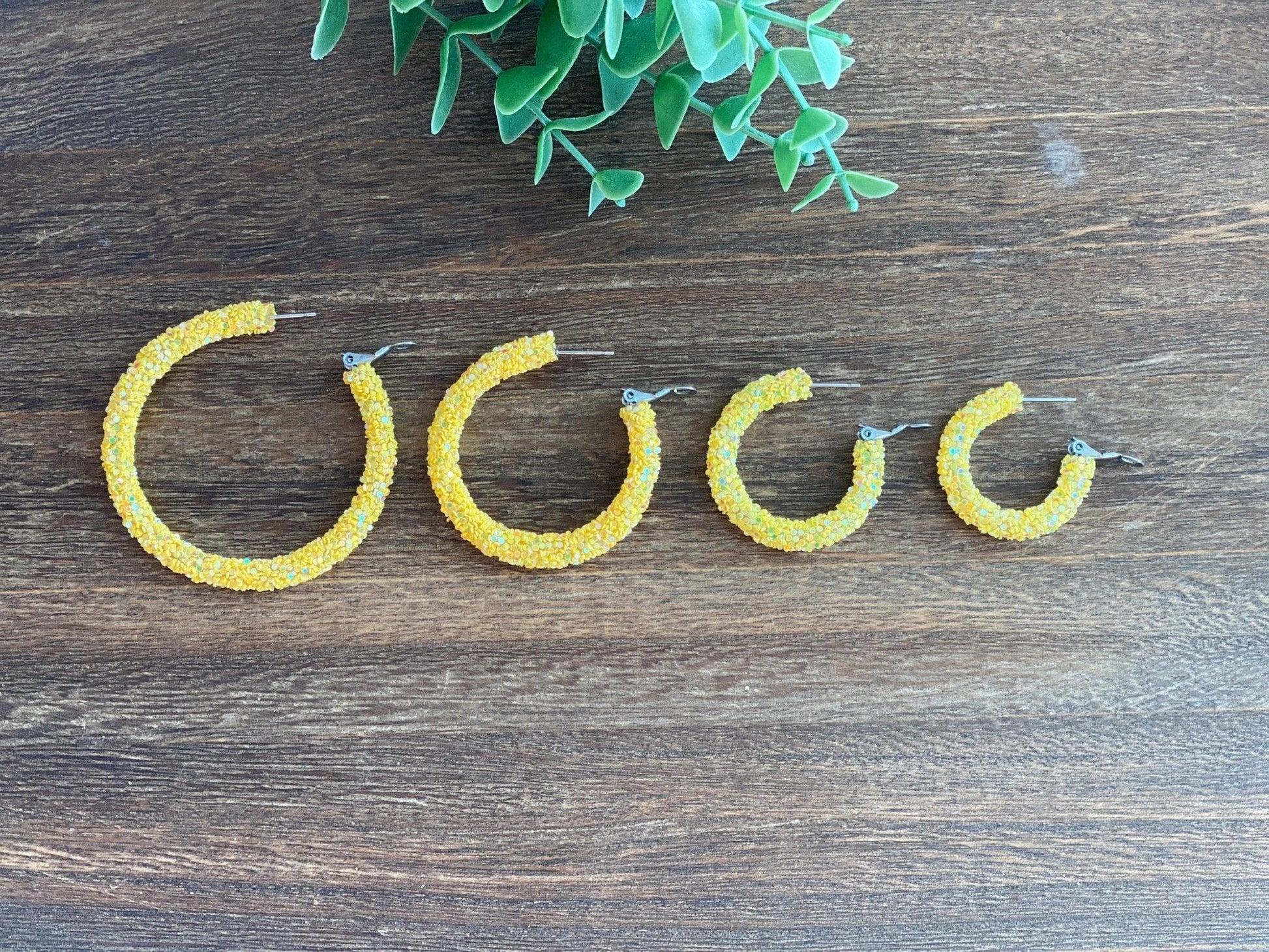 Four Different Sizes of Handmade Sparkly Yellow Leverback Hoops Lined Up on Dark Wood Display