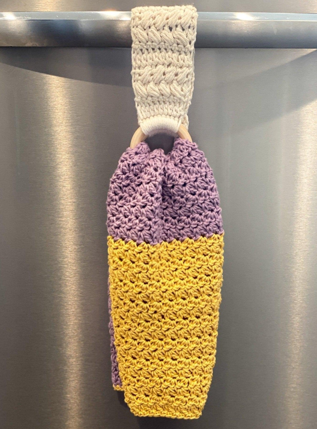 purple and gold crocheted dish towel hanging in crochet towel holder on dishwasher handle