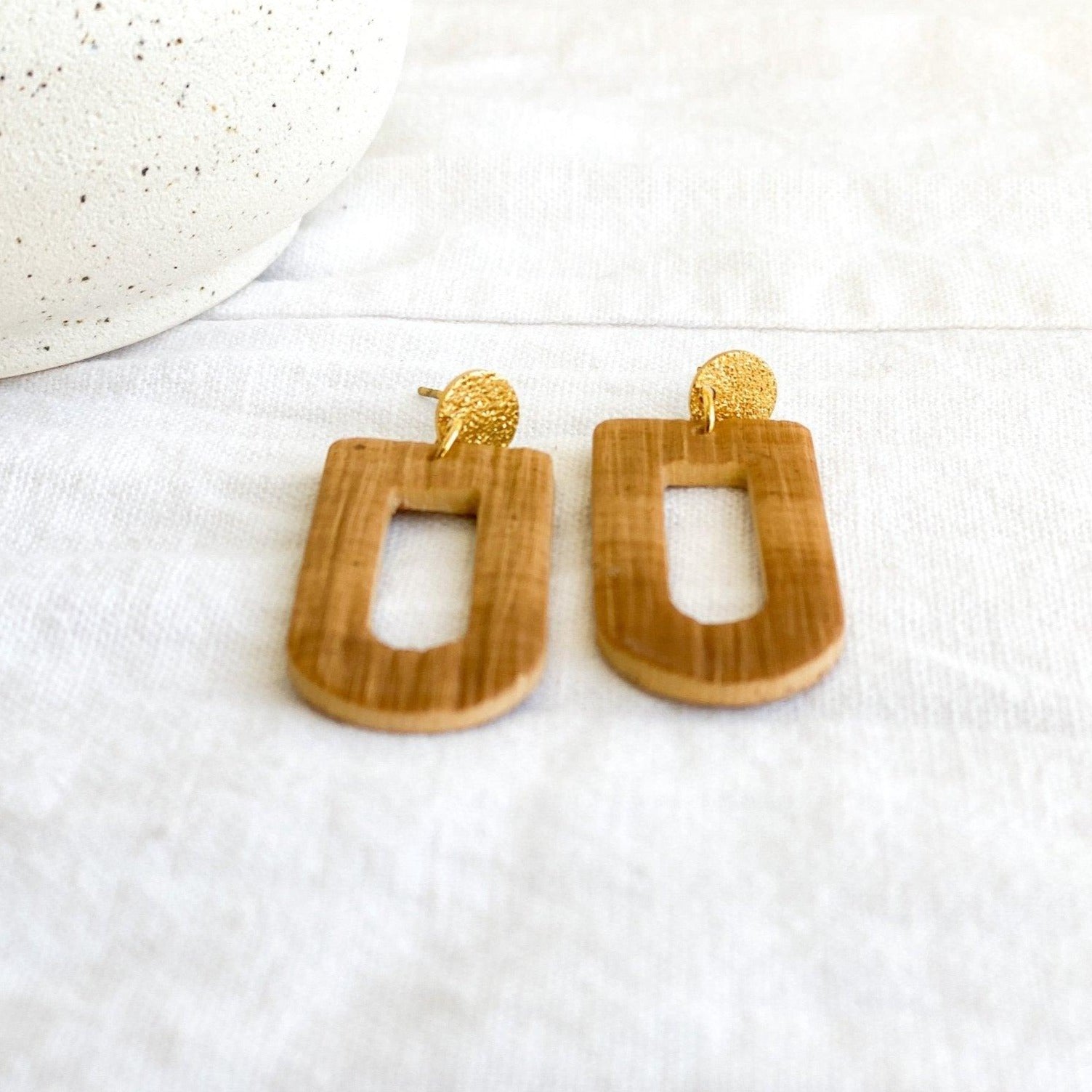 cute handmade brown earrings with gold surgical steel posts laying on white cloth next to white vase