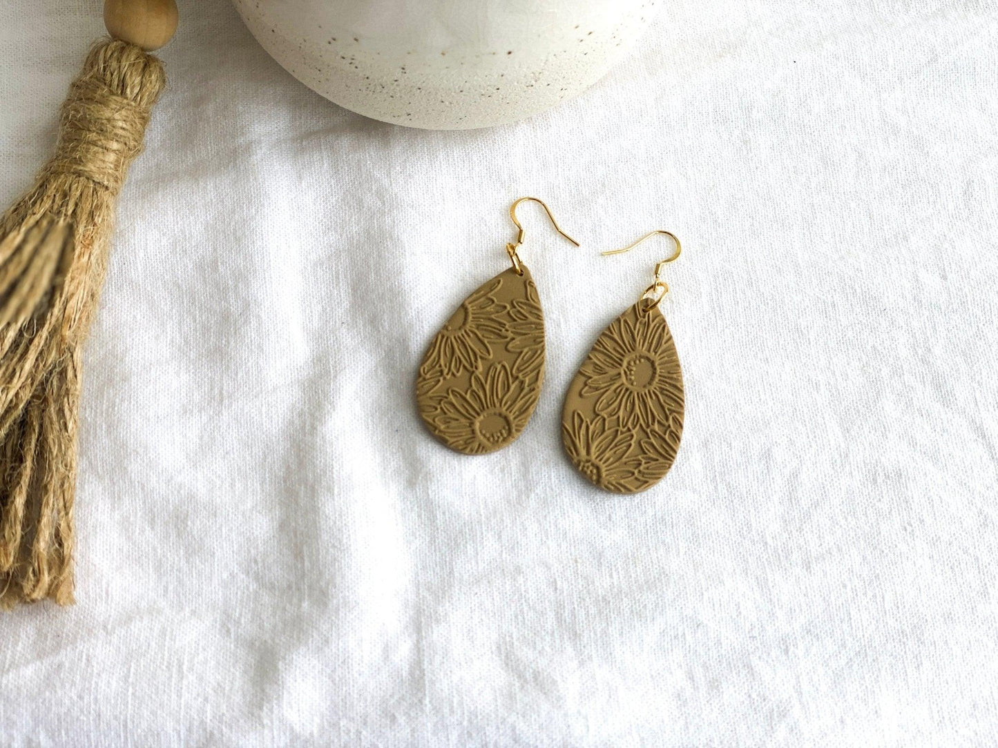 Handmade, Neutral Color Teardrop Shaped Earrings with Embossed Daisy Print with Gold Surgical Steel Ear Wires on White Cloth