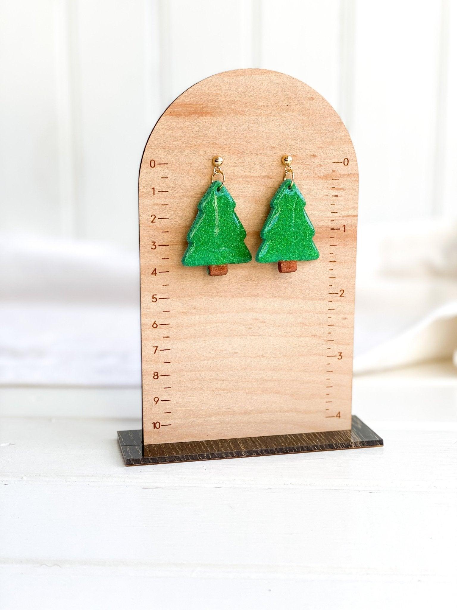 handmade earrings that are sparkly green christmas trees attached to gold ball posts on earring card on measurement stand