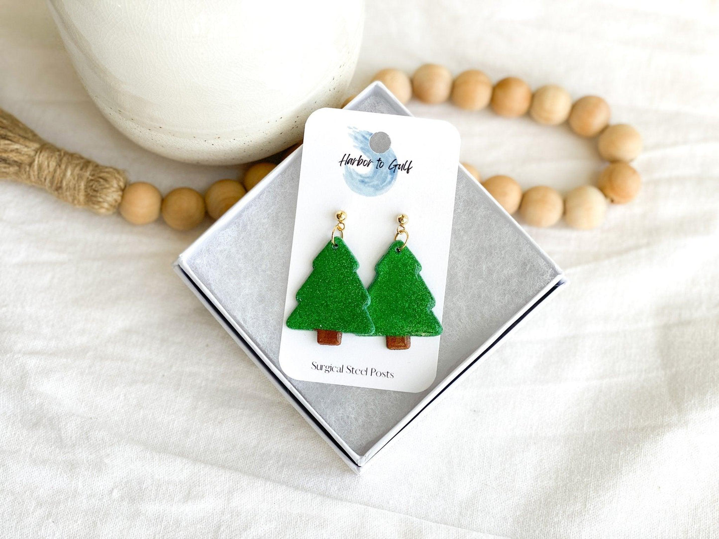 handmade earrings that are sparkly green christmas trees attached to gold ball posts on earring card in white gift box