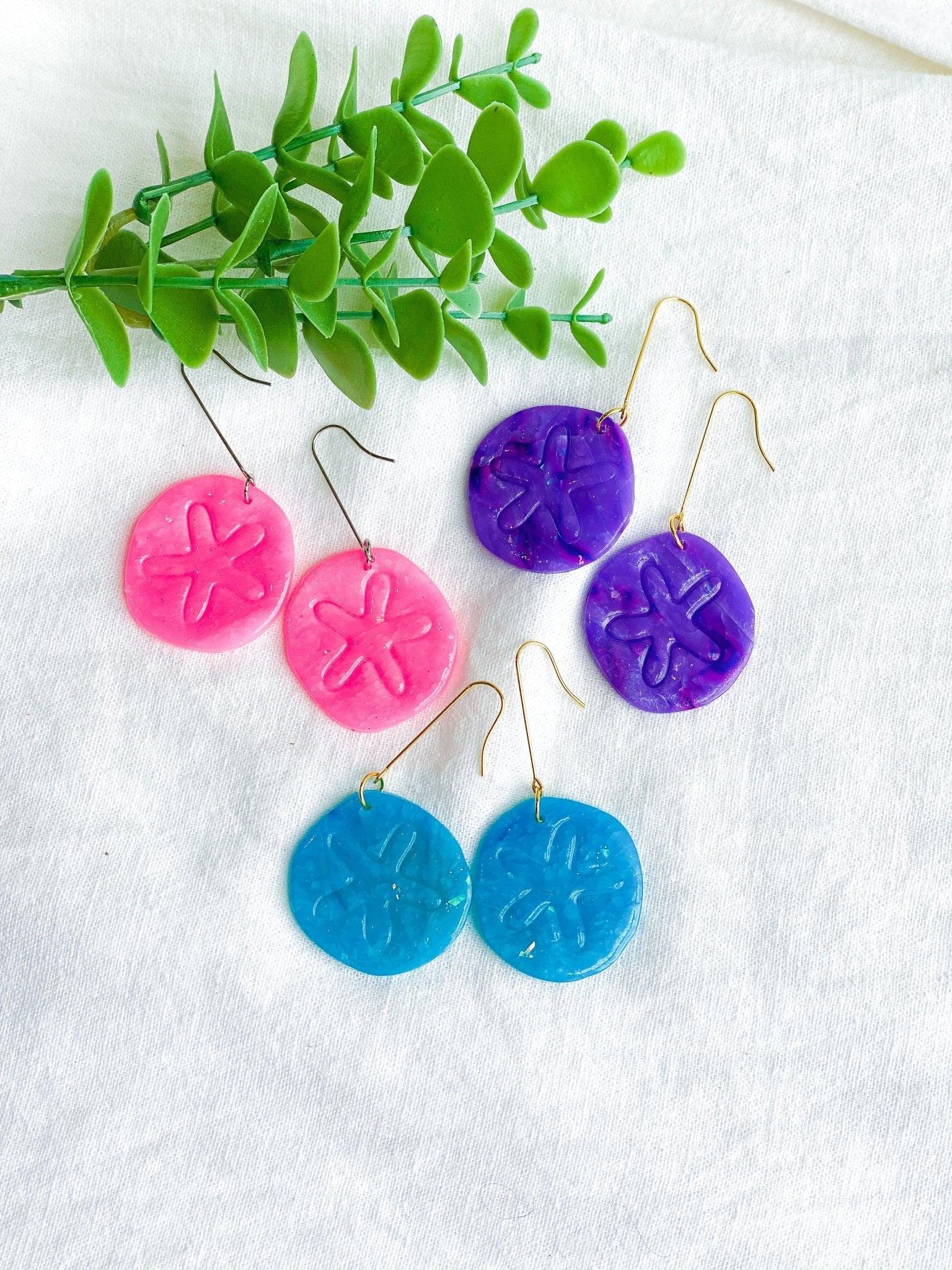 Three Pairs of Handmade Bright Colored Sand Dollar Earrings on Long Surgical Steel Ear Wires laying flat on white linen cloth