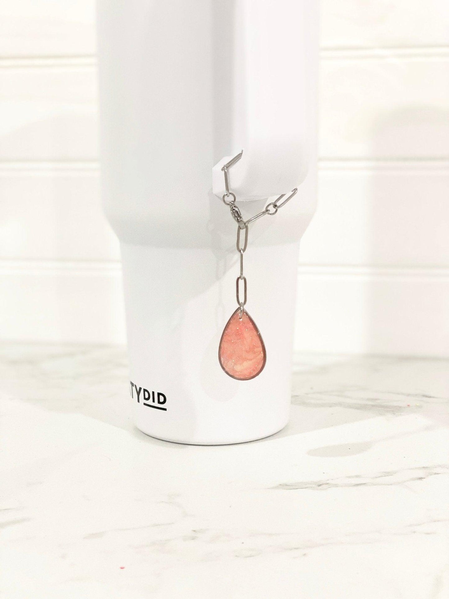 Pink Teardrop Stanley Cup Charm Attached To Silver Stainless Steel Chain On Handle Of White Stanley Cup