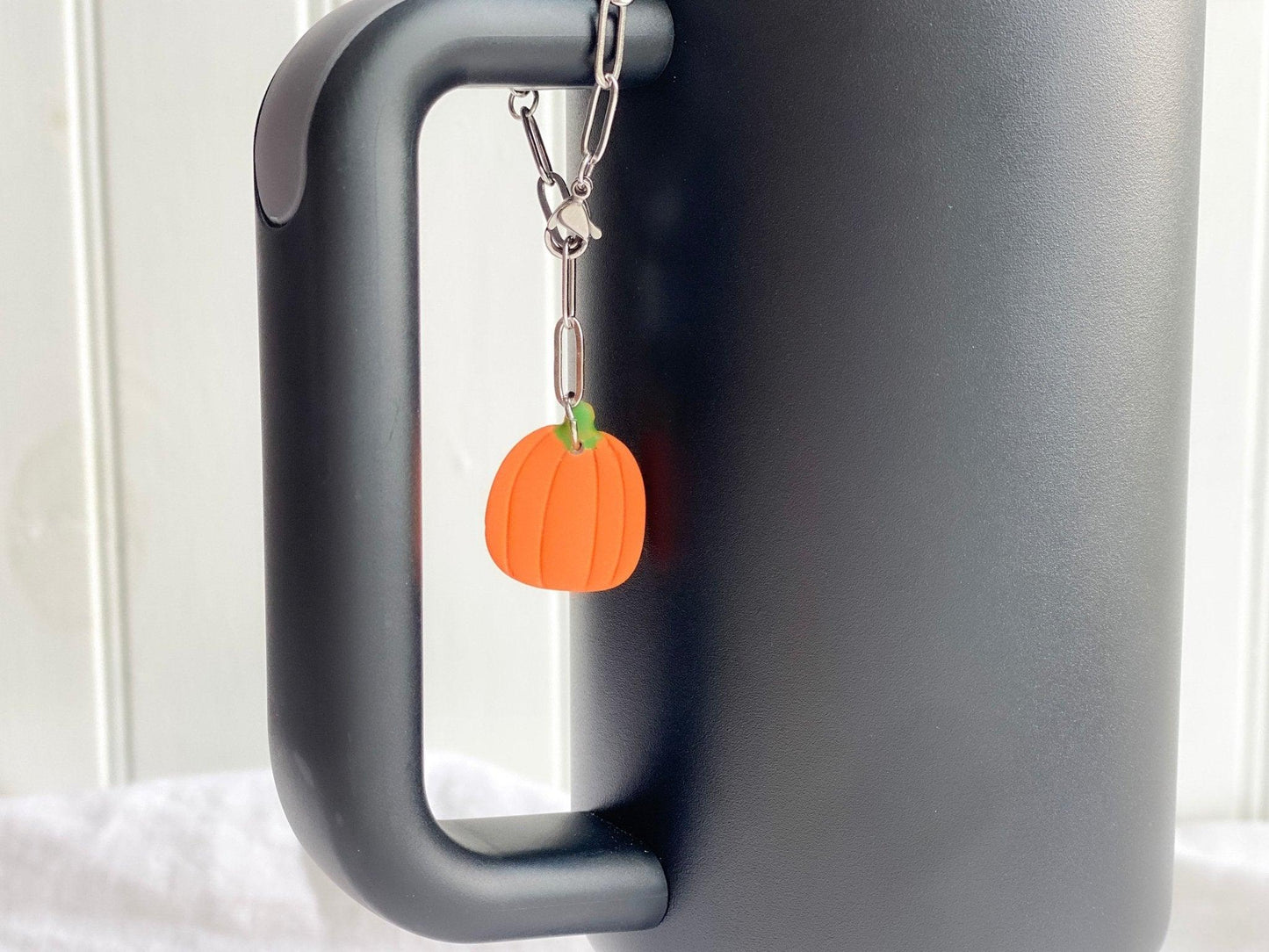 Pumpkin Stanley Cup Charm Attached To Silver Stainless Steel Chain On Handle Of A Black Stanley Cup