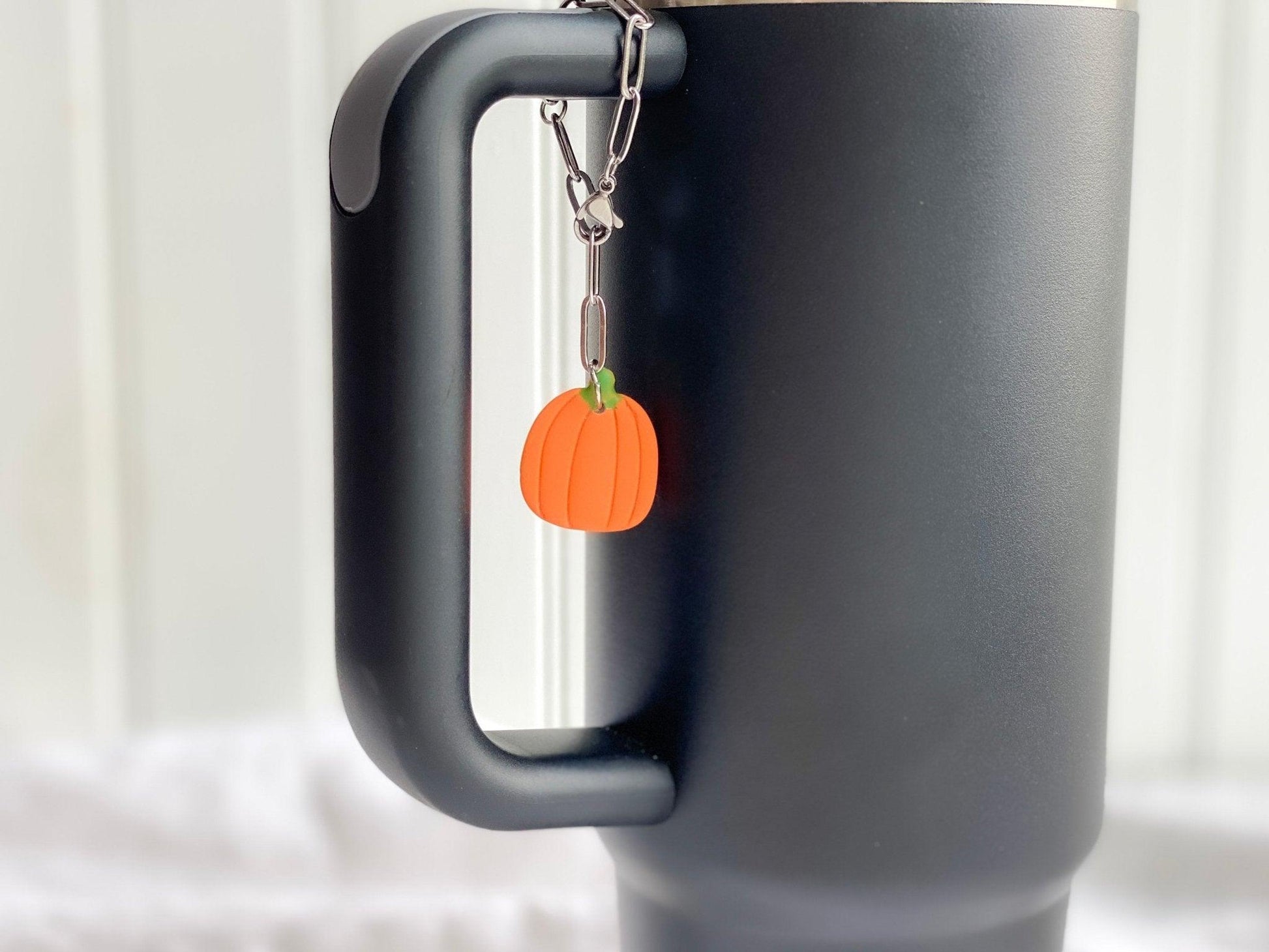 Pumpkin Stanley Cup Charm Attached To Silver Stainless Steel Chain On Handle Of A Black Stanley Cup