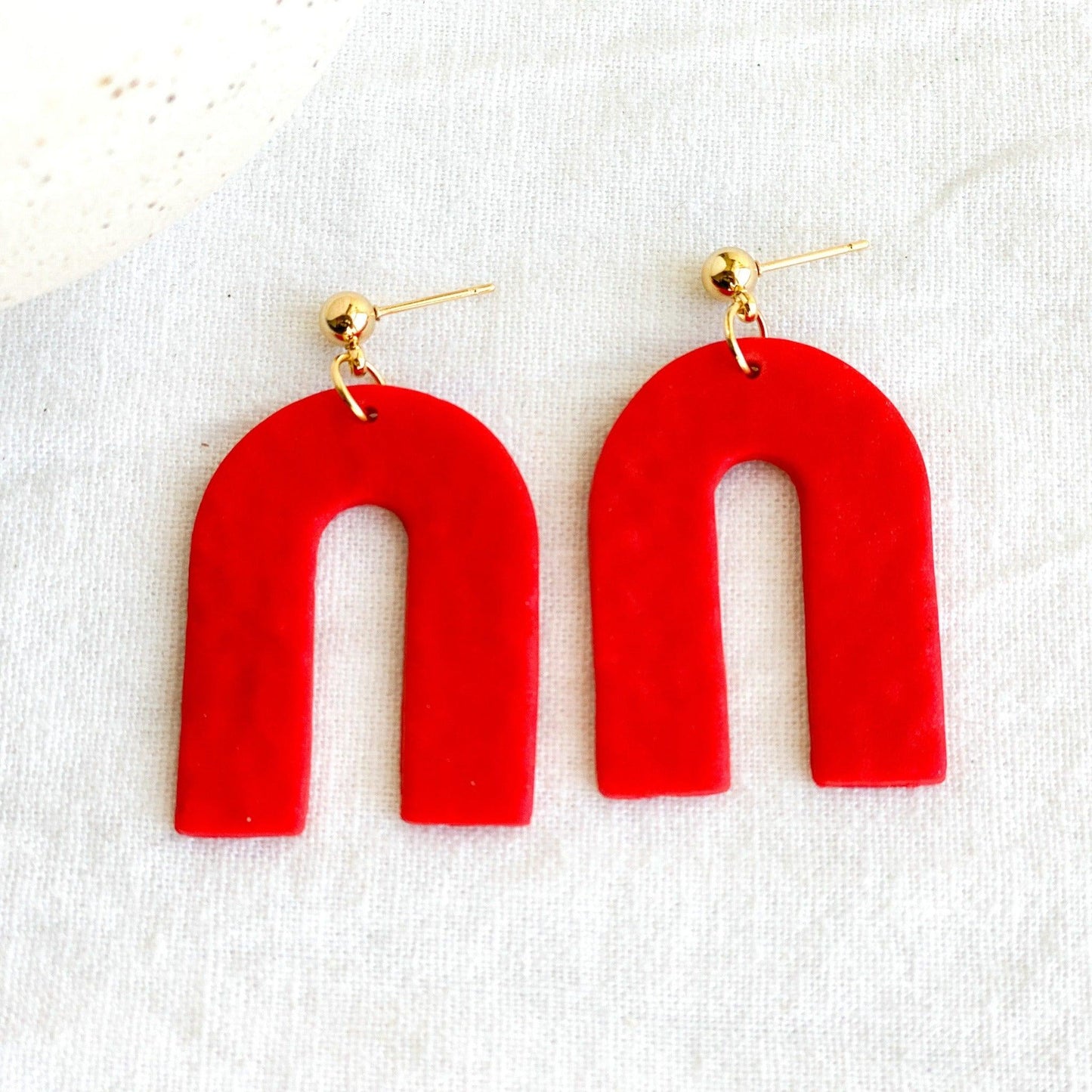 Close Up of Textured Handmade Bright Red Earrings with Gold Surgical Steel Ball Posts Laying Flat on White Linen Cloth