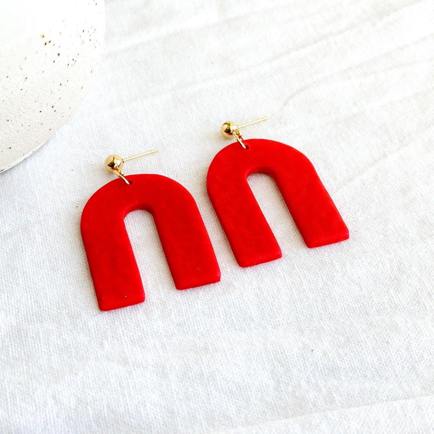 Textured Handmade Bright Red Earrings with Gold Surgical Steel Ball Posts Laying Flat on White Linen Cloth