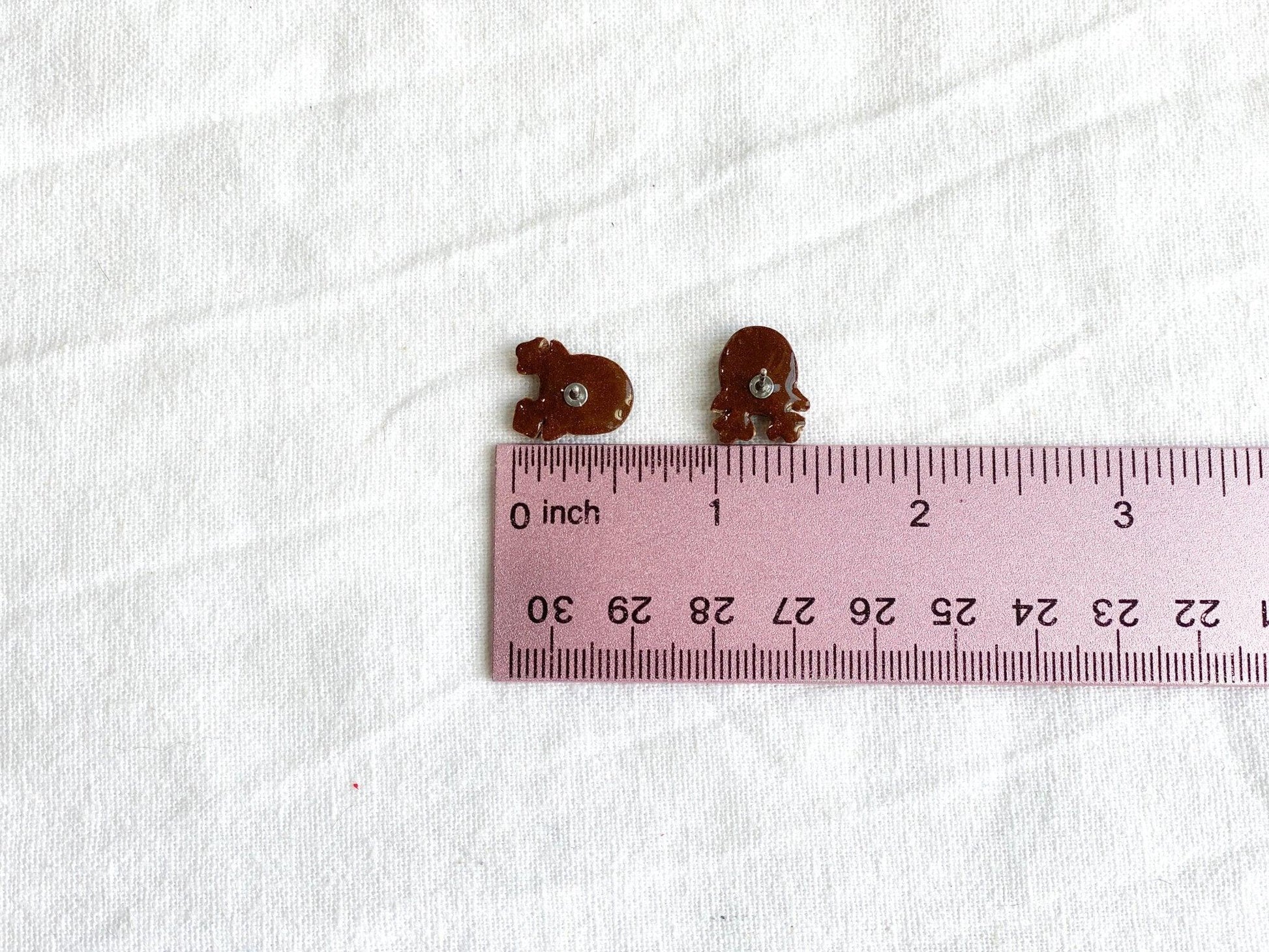 Cute handmade Rudolph Stud Earrings made from polymer clay and surgical steel posts on white cloth next to pink ruler