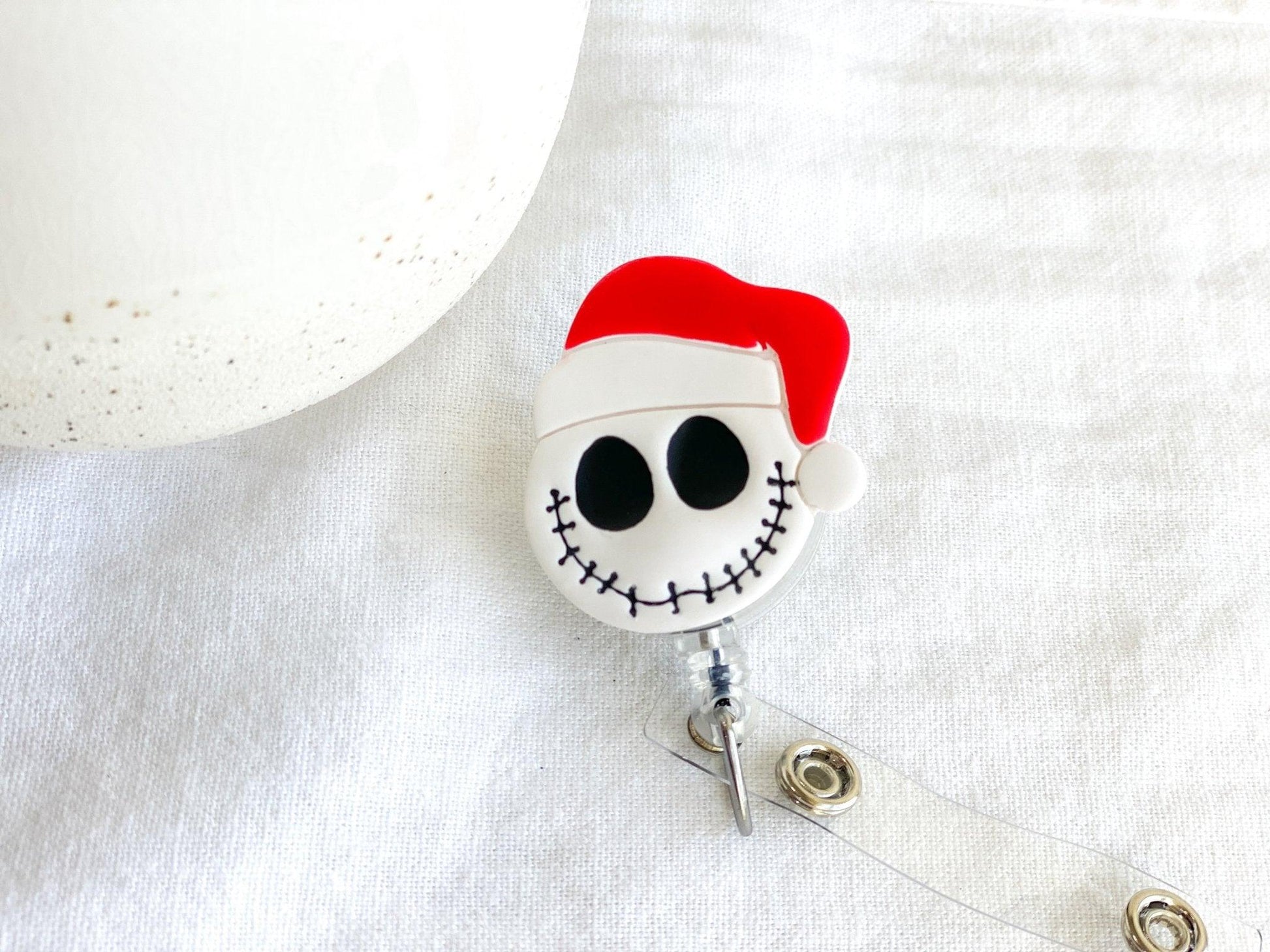 Close Up of Handmade Santa Claus Jack Skellington Retractable Badge Reel laying on white cloth next to white vase