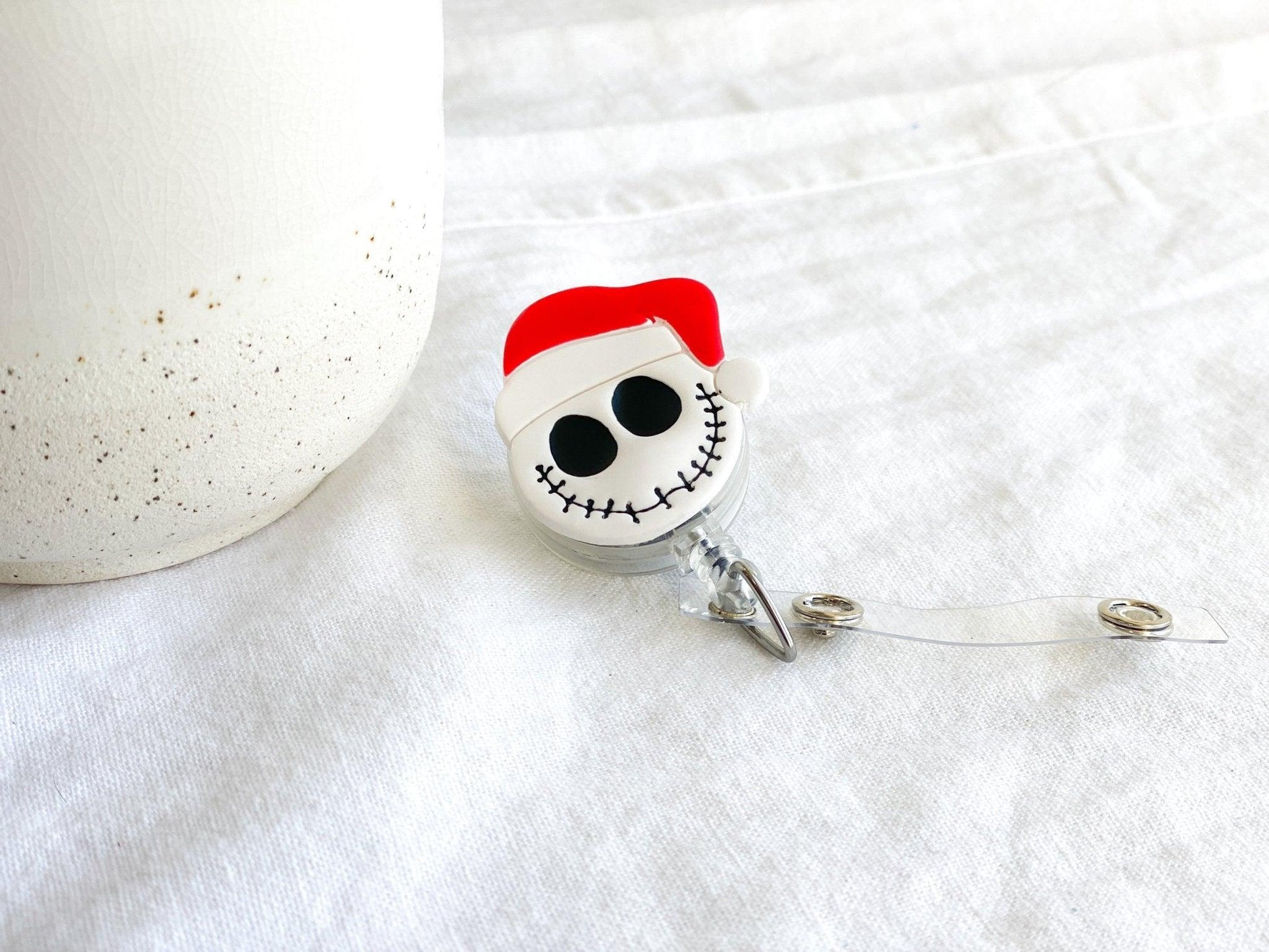 Close Up of Handmade Santa Claus Jack Skellington Retractable Badge Reel laying on white cloth next to white vase