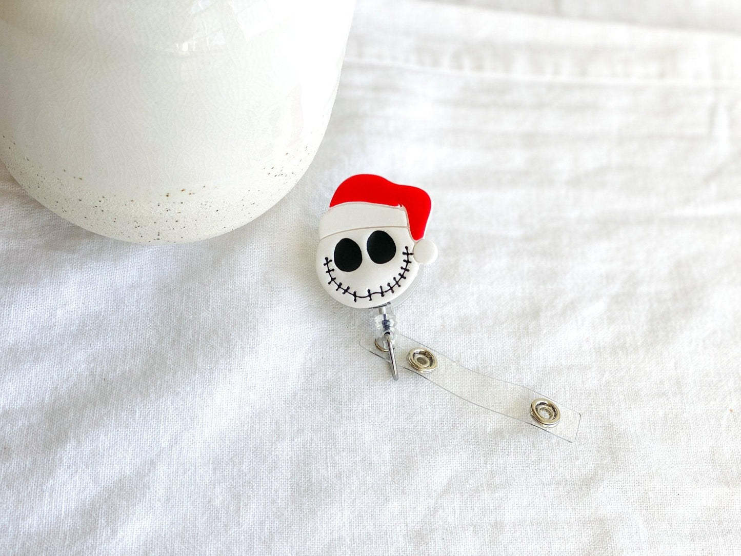 Handmade Santa Claus Jack Skellington Retractable Badge Reel laying on white cloth next to white vase