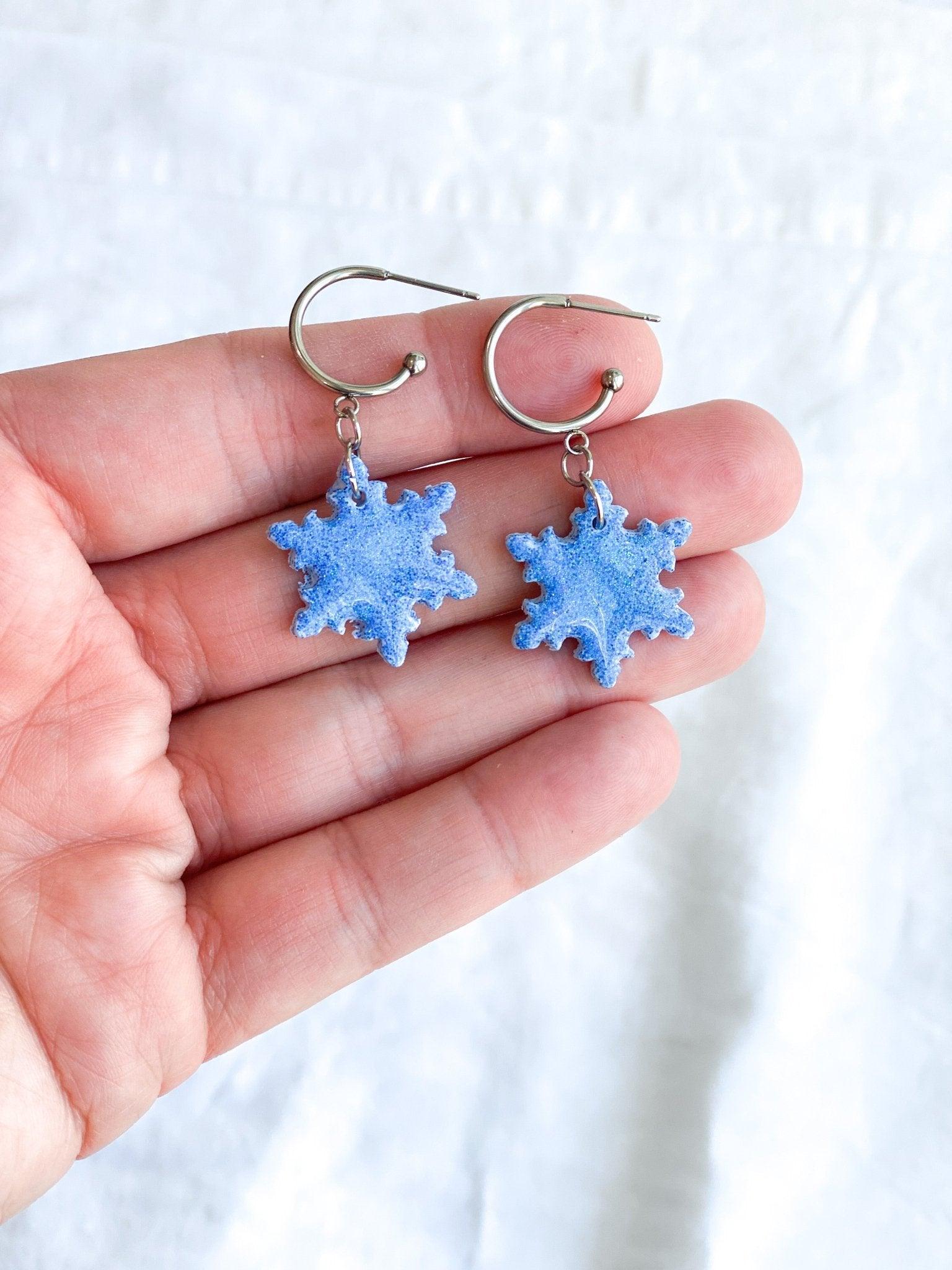 Handmade Sparkly Blue Snowflake Earrings on Silver Surgical Steel Huggie Earrings being held in human hand