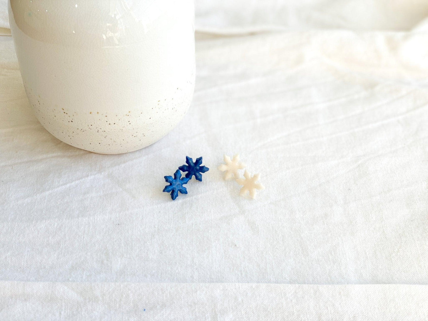 Handmade Snowflake Stud Earrings with Surgical Steel Posts in Blue and White on White Linen Cloth