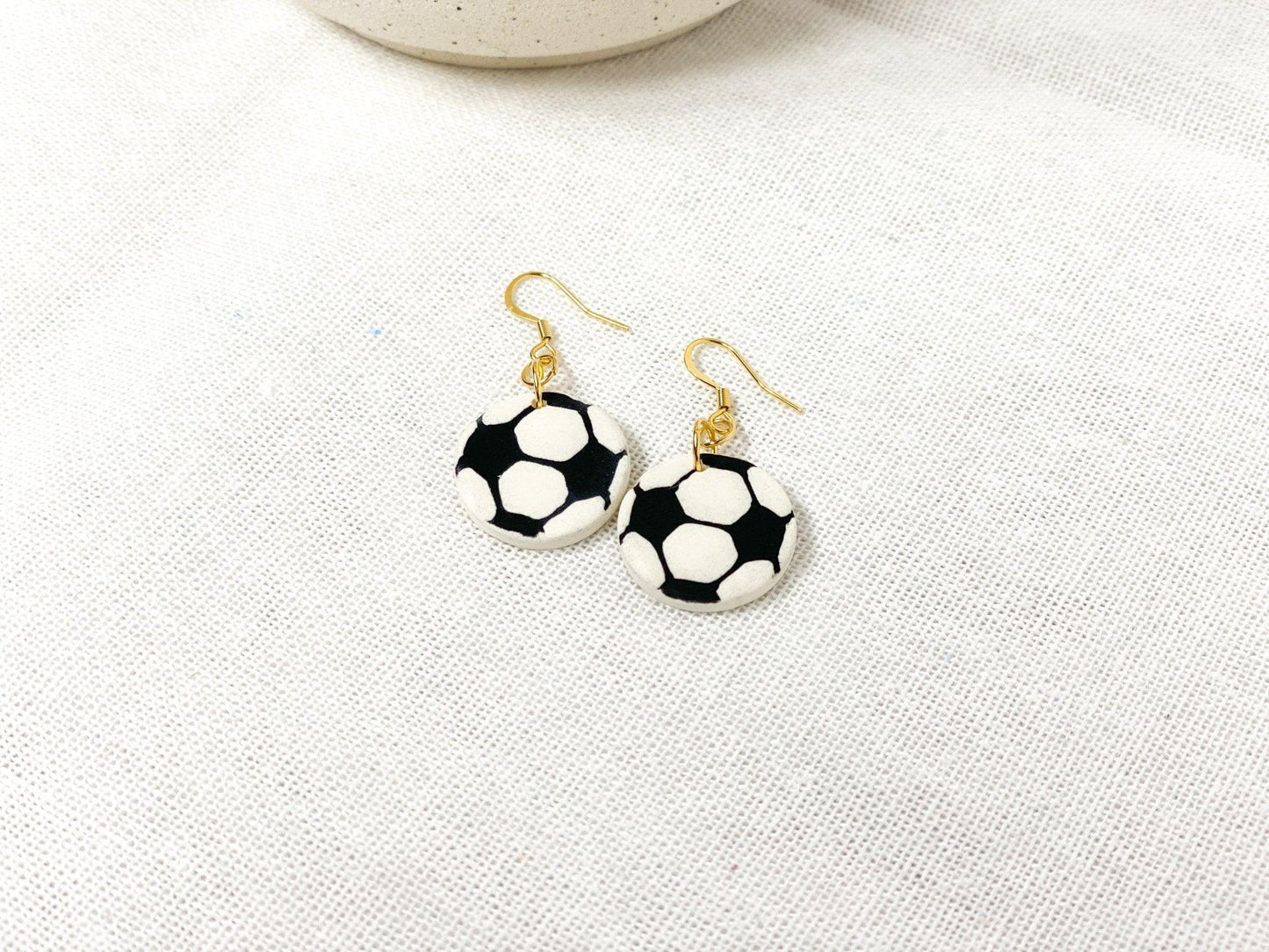 Handmade Soccer Earrings with Gold Surgical Steel Ear Wires laying flat on White Linen Cloth