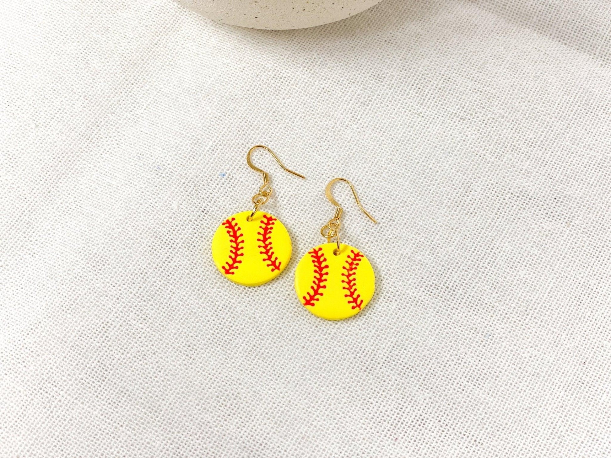 Handmade Softball Earrings with Gold Surgical Steel Ear Wires laying flat on White Linen Cloth