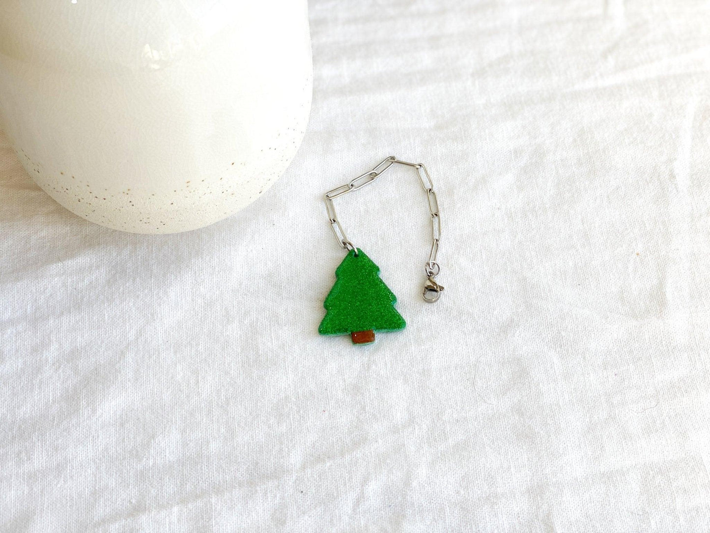 Sparkly Green Christmas Tree Stanley Cup Charm Attached To Silver Stainless Steel Chain Laying Flat On White Cloth