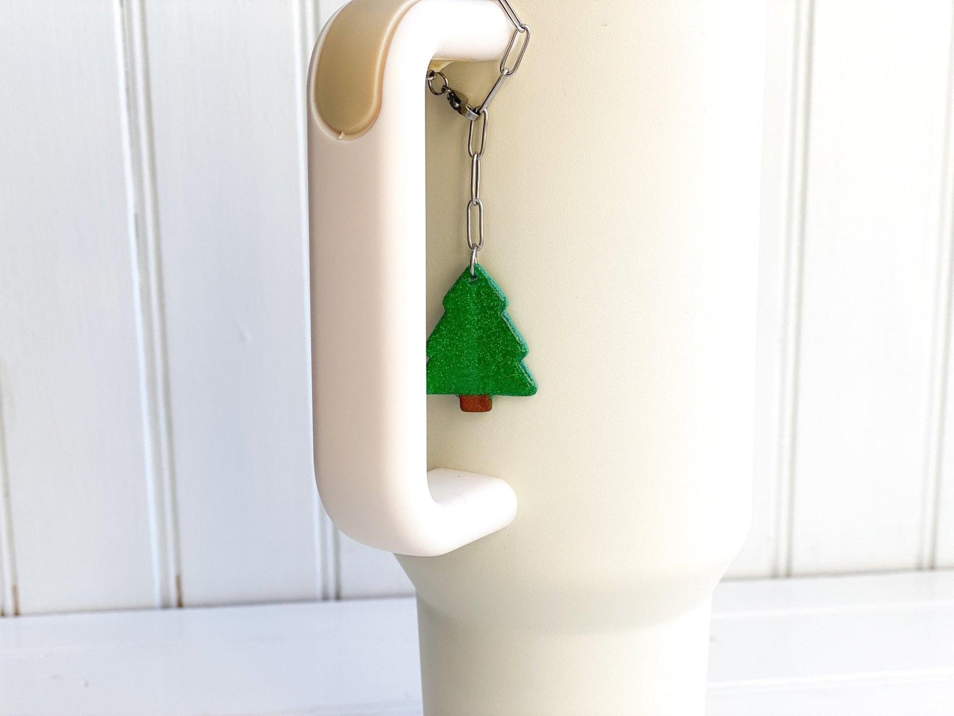 Sparkly Green Christmas Tree Stanley Cup Charm Attached To Silver Stainless Steel Chain On Handle Of White Stanley Cup