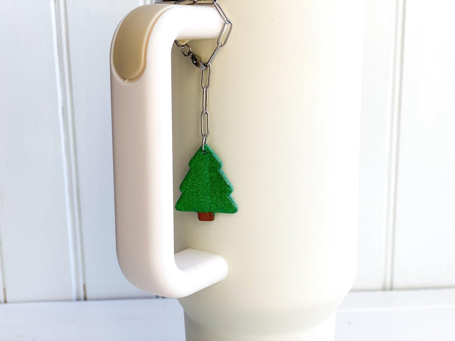 Sparkly Green Christmas Tree Stanley Cup Charm Attached To Silver Stainless Steel Chain On Handle Of White Stanley Cup