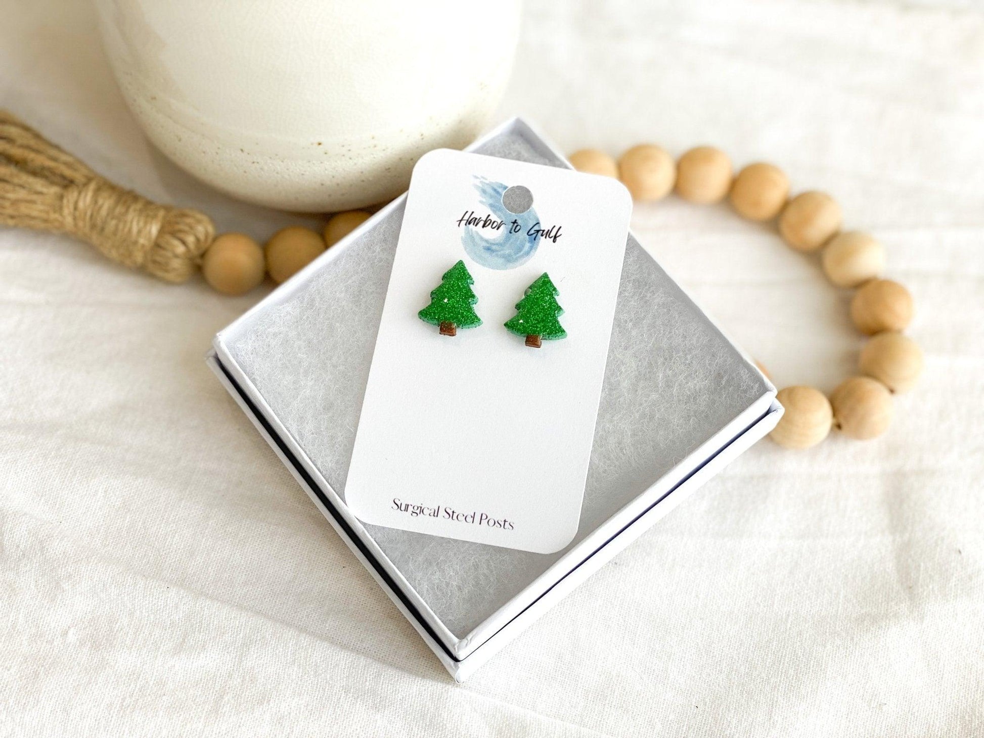 Small Handmade Green Sparkly Christmas Tree Stud Earrings on White Earring Card in White Gift Box propped on wooden beads