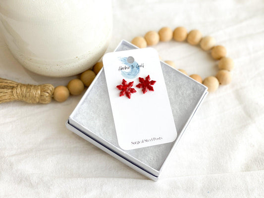 Small Handmade Red Sparkly Snowflake Stud Earrings on wihte earring card in white gift box propped on strand of wood beads