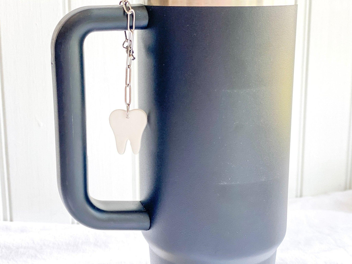 White Tooth Stanley Cup Charm Attached To Silver Stainless Steel Chain On Handle Of A Black Stanley Cup