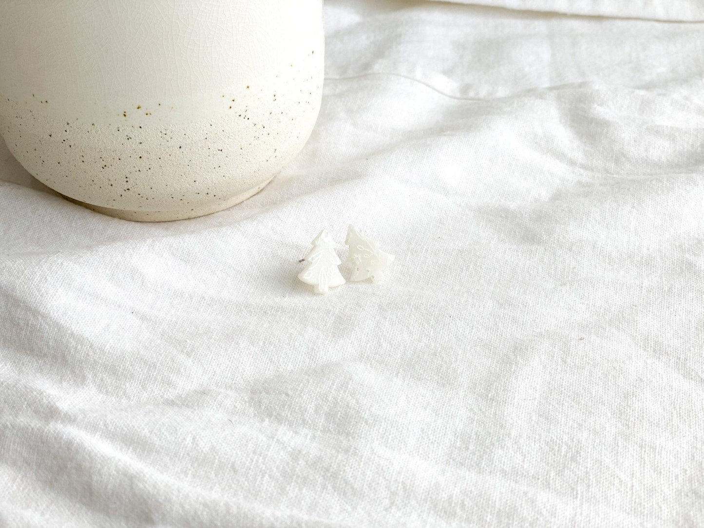 Small Handmade White Christmas Tree Stud Earrings with Surgical Steel Posts  on White Linen Cloth Next to White Vase