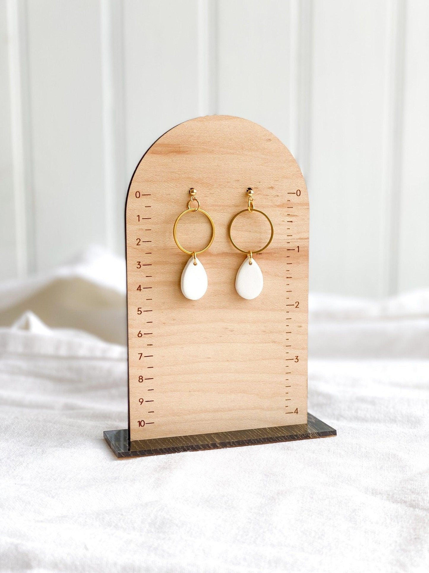 handmade white tear drops attached to thin open gold circles on gold ball posts on wood measurement stand