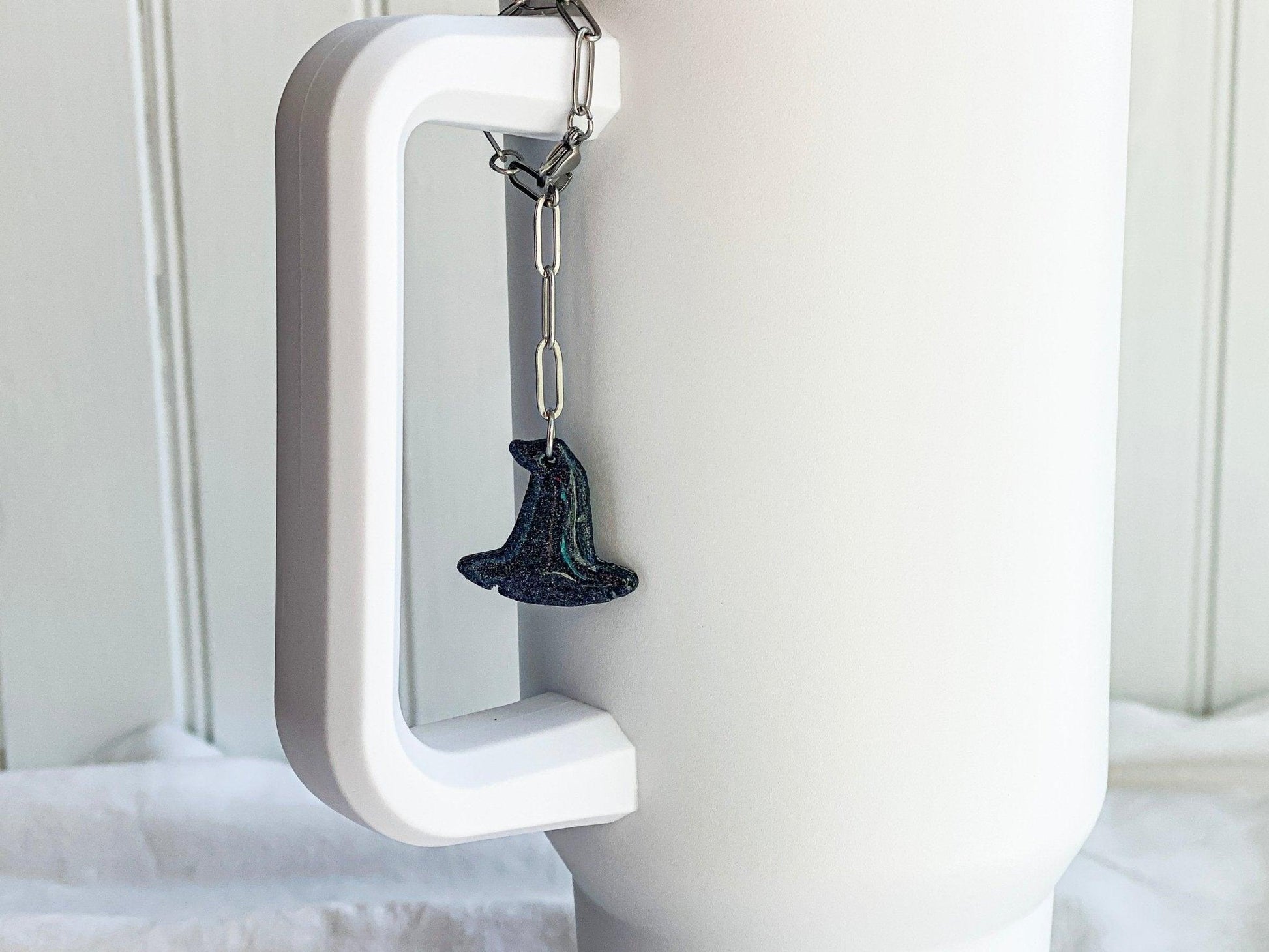 Sparkly Black Witch Hat Stanley Cup Charm Attached To Silver Stainless Steel Chain On Handle Of White Stanley Cup